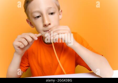 Un garçon dans un T-shirt orange mord une bande de papier multicolore fin Banque D'Images