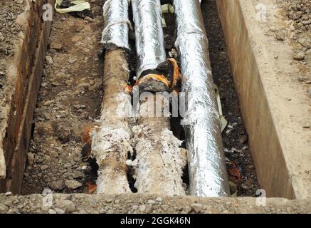 Réparation, isolation et remplacement des égouts urbains dans la rue. Tuyaux d'eau dans une tranchée de terre. Banque D'Images