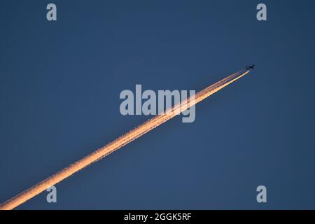 Belle vue en soirée avec téléobjectif de l'avion contrail dans les couleurs orange de coucher du soleil sur fond bleu foncé vu au-dessus des montagnes de Dublin, Irlande Banque D'Images