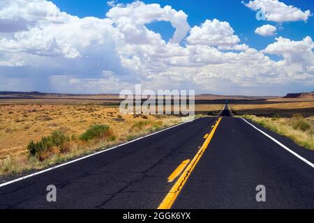 Vue sur la route asphaltée noire sans fin vide avec des marquages de voie jaune et blanc dans le paysage aride sec contre ciel bleu d'été avec cumulus nuages - Arizo Banque D'Images
