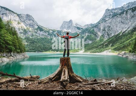 Heureux voyageur debout sur une souche d'arbre en admirant les montagnes du pic de Dachstein sur un lac supérieur de Gosau. Gosau, Salzkammergut, Autriche, Europe. Banque D'Images