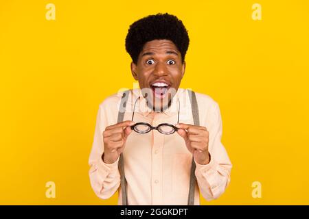 Photo de surprise fou excités gars enlever les spécifications port bretelles chemise isolé couleur jaune arrière-plan Banque D'Images