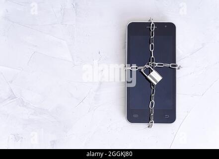 Vue de dessus d'un smartphone enveloppé d'un verrou de chaîne sur une table en béton. Concept de sécurité mobile. Banque D'Images