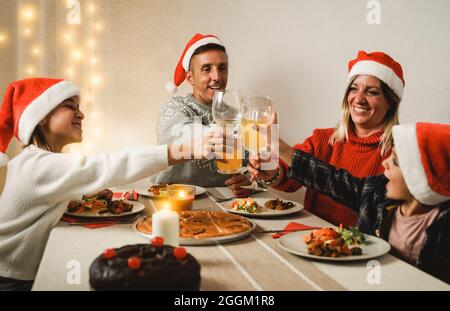 Bonne famille qui s'amuse à célébrer Noël manger un dîner végétalien ensemble à la maison - concentrez-vous sur le père portant des chapeaux de Santa Clause Banque D'Images