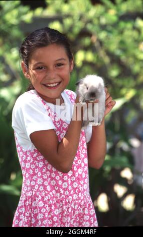 Austin Texas USA,1995: Fille hispanique de 9 ans tient doucement son lapin de lapin d'animal de compagnie dans l'arrière-cour de sa famille. M. EC-0089 ©Bob Daemmrich Banque D'Images