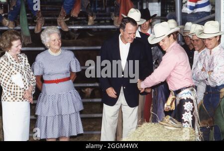 Houston Texas USA, 12 juillet 1990: Le président américain George H.W.Bush se serre la main avec un cow-boy lors d'un rodéo de style texan, organisé pour les participants au Sommet économique des nations industrialisées, qui a réuni des dirigeants du monde entier.La première ministre britannique Margaret Thatcher se trouve à gauche et la première dame Barbara Bush est au milieu.©Bob Daemmrich Banque D'Images
