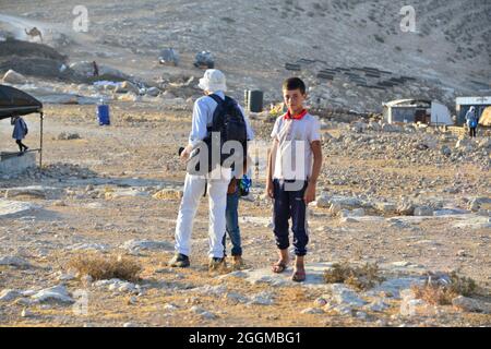 Depuis 2004, les enfants du village de Tuba se mettent à l'école dans le village voisin d'AT-Tuwani, A 2.6 km - tout en étant chaperé par un militant juif et un véhicule des forces de défense israéliennes afin des protéger des attaques violentes des colons juifs religieux contre l'avant-poste illégal de Maon Farm qui se trouve sur leur chemin vers l'école. Palestine / Israël, au sud d'Hébron. 31 août 2021. (Photo par Matan Golan/Alay Live News) Banque D'Images