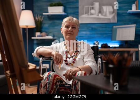 Portrait d'un vieil artiste handicapé assis dans un studio d'art à la maison. Femme aînée avec un handicap en fauteuil roulant se préparant pour le dessin de chef-d'œuvre comme passe-temps. Personne âgée handicapée Banque D'Images