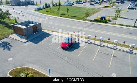 Tesla modèle S garée et en charge à une station de Supercharger de Tesla dans un centre-ville, vue d'en haut par drone. Banque D'Images