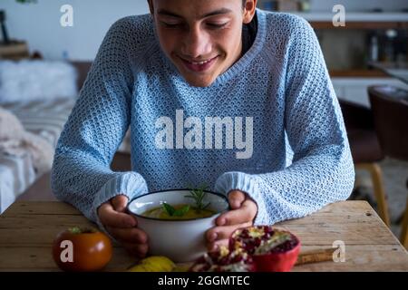 Jeune garçon adolescent sourire en regardant une soupe de légumes à la maison pendant le déjeuner - végétarien et saine alimentation concept de nutrition mode de vie - les gens de garçon et au Banque D'Images