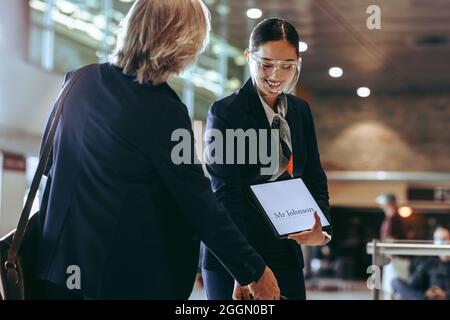 Une femme pilote portant un masque de protection avec une plaque signalétique recevant un voyageur. Chauffeur avec une pancarte sur le point d'arrivée de l'aéroport recevant l'homme d'affaires. Banque D'Images