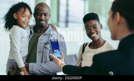 Le personnel de l'aéroport s'est assuré de la carte d'embarquement numérique sur le téléphone de la famille touristique au comptoir d'enregistrement. Un employé de la compagnie aérienne vérifie la carte d'embarquement du passager Banque D'Images