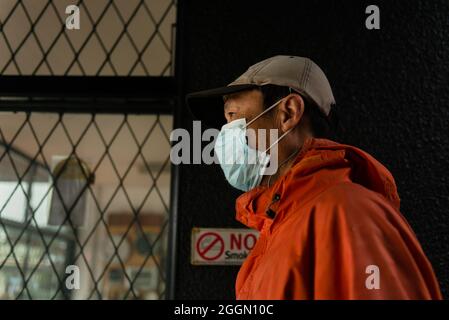 Homme portant un masque de visage passant devant un magasin fermé avec une porte de sécurité en acier. Panneau interdiction de fumer à côté de la porte du magasin. Banque D'Images