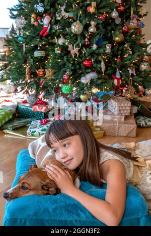 Fille de huit ans qui pose avec son chien devant l'arbre de Noël Banque D'Images