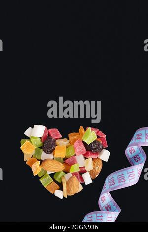 Concept alimentaire pour la Saint-Valentin. Concept amincissant. Fruits secs et noix en forme de coeur et ruban de mesure isolé sur fond noir, copie de spac Banque D'Images