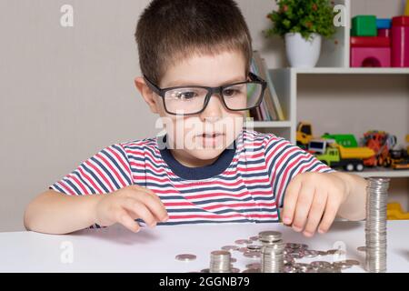 Un enfant en lunettes, un jeune homme d'affaires joue avec des pièces de monnaie et économise de l'argent. Banque D'Images