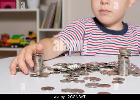 Un enfant en lunettes, un jeune homme d'affaires joue avec des pièces de monnaie et économise de l'argent. Banque D'Images