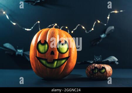 Halloween. Deux grandes et petites citrouilles colorées et des chauves-souris en papier. Arrière-plan sombre avec des lumières. Lanterne de Jack décorée par des enfants. Banque D'Images