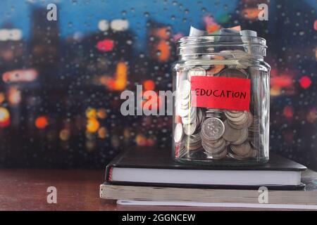 Pièces de monnaie en verre étiquette pot avec éducation et livre sur table en bois. Concept financier. Banque D'Images