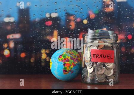 Concept de budget de voyage. Pièces de monnaie dans un pot en verre et globe terrestre avec espace de copie pour le texte Banque D'Images