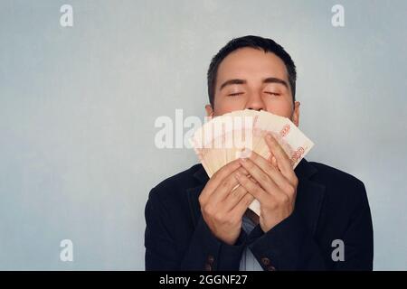 Homme sniffing dollars. La douce odeur de l'argent. Un jeune gars qui a renifé 5000 roubles a gagné de l'argent. Salaire. Argent facile. Un paquet d'argent Banque D'Images