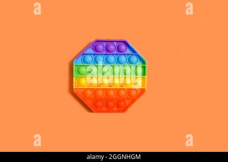 Nouveau jouet antistress pop IT coloré pour enfant sur fond orange isolé. Vue de dessus, espace de copie. Banque D'Images