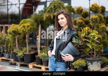 Une jeune jolie fille, vêtue d'une veste en cuir et d'un Jean, se tient près du centre de la fleur et tient un grand beau pot de fleurs Banque D'Images