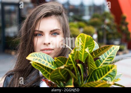 Une jeune jolie fille, vêtue d'une veste en cuir et d'un Jean, se tient près du centre de la fleur et tient un grand beau pot de fleurs Banque D'Images