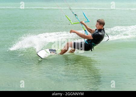 Jeune adulte de type caucasien homme personne appréciez l'équitation kite surf planche dans soleil protection uv costume le jour lumineux ensoleillé contre le ciel bleu à la mer ou l'océan Banque D'Images