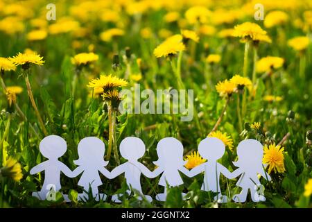 Silhouettes d'enfants tenant les mains coupées en carton sur un fond de pissenlits. Filles et garçons en papier blanc. Enfants internationaux Banque D'Images