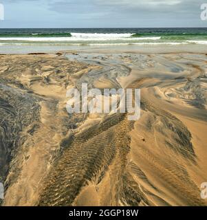 Détails fluviaux sur une plage où la tourbe est lavée dans le sable et la marée crée de beaux motifs. Reef Beach dans l'île de Lewis. Banque D'Images