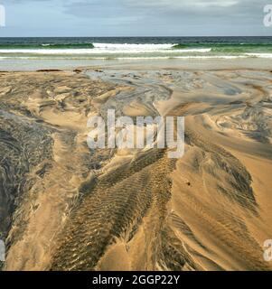 Détails fluviaux sur une plage où la tourbe est lavée dans le sable et la marée crée de beaux motifs. Reef Beach dans l'île de Lewis. Banque D'Images