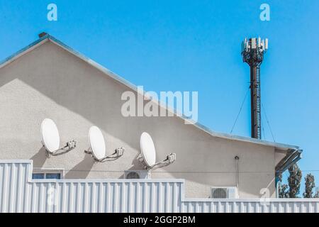 Télévision par satellite, blanc, antenne et communications sur le mur d'un immeuble résidentiel sur fond de ciel bleu et Internet towe Banque D'Images