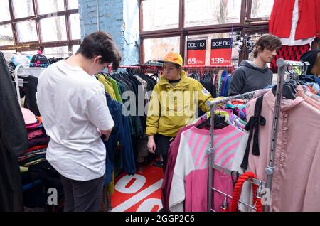 Marché aux puces. Jeune homme choisissant des vêtements de seconde main dans un magasin, femme vendeur l'aidant. 26 septembre 2019. Kiev, Ukraine Banque D'Images