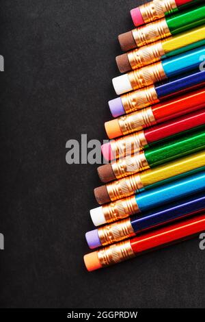 Crayons colorés avec gommes à effacer sur un fond noir. Vue de dessus, espace libre Banque D'Images