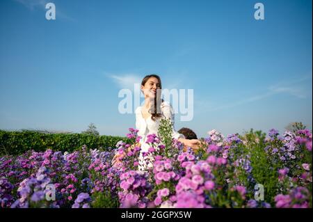 Belle jeune femme asiatique en robe blanche appréciant la fleur de margaret floraison dans le jardin sur ensoleillé Banque D'Images