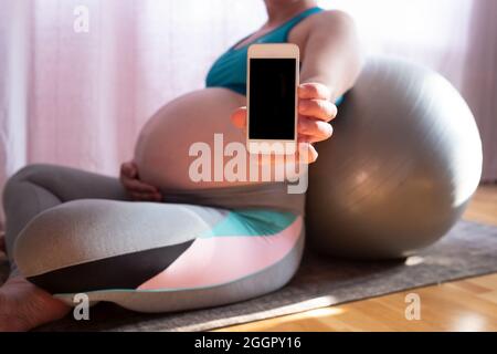 Une jeune femme enceinte affiche un téléphone portable avec écran noir après un entraînement sportif Banque D'Images