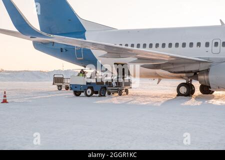 chargement des bagages à l'aéroport en hiver. Bagages dans les chariots près de l'avion en hiver. Avion passager en hiver à l'aéroport a chargé des bagages avant le départ Banque D'Images