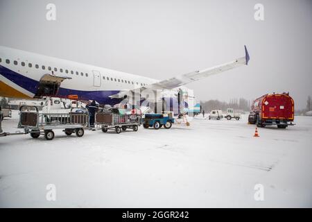 chargement des bagages à l'aéroport en hiver. Bagages dans les chariots près de l'avion en hiver. Avion passager en hiver à l'aéroport a chargé des bagages avant le départ Banque D'Images