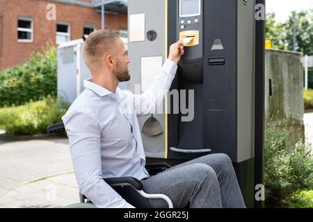 Homme handicapé en fauteuil roulant payant un ticket de parking utilisant la machine Banque D'Images