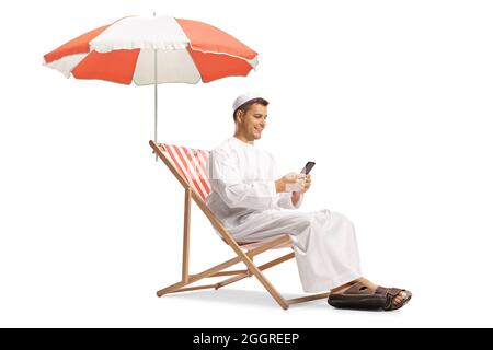 Jeune homme dans des vêtements ethniques assis sous un parapluie et utilisant sur un téléphone portable isolé sur fond blanc Banque D'Images