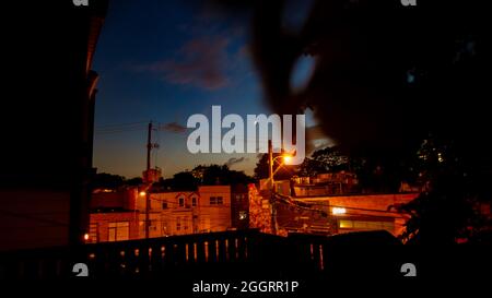 Lumières orange de la ville, fenêtres, rues sous bleu et coucher de soleil cramoisi ciel avec croissant de lune Banque D'Images