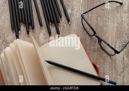 carnet ouvert avec crayons et lunettes de couleur sur une table texturée en bois, instruments dans l'espace de travail, détail des objets artistiques Banque D'Images