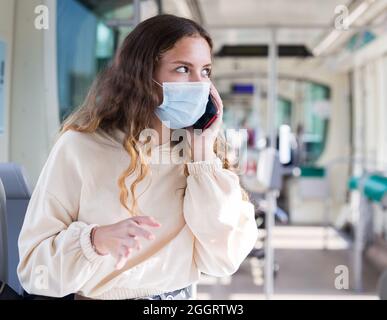 Femme en masque utilisant un téléphone portable sur le chemin de travail en tram Banque D'Images