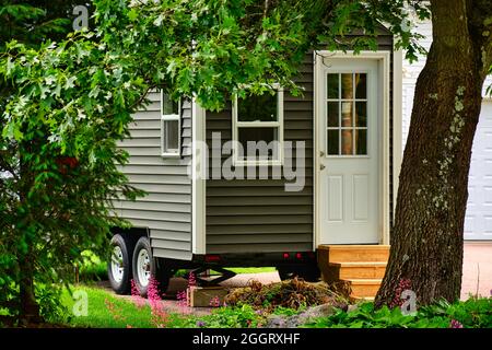 Petite maison sur roues encadrées par des arbres et des fleurs Banque D'Images