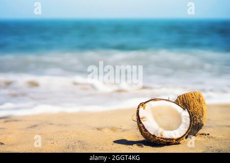 Deux moitiés d'une noix de coco mûre dans le coin de la composition. Noyer se trouve sur une plage de sable blanc sur fond flou de mer bleue et ciel bleu avec c Banque D'Images