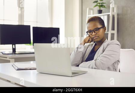 Femme d'affaires sérieuse et attentionnés, assise au bureau et regardant l'écran d'un ordinateur portable Banque D'Images