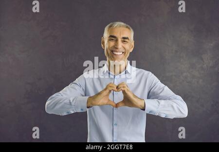 Le portrait de l'homme sur fond noir montre le geste du coeur Banque D'Images