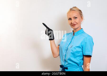 Une jeune femme en uniforme et gants en caoutchouc pointe son doigt vers la gauche. Copier l'espace. Travailleur médical, cosmétologue et médecin. Le concept de bustiin Banque D'Images