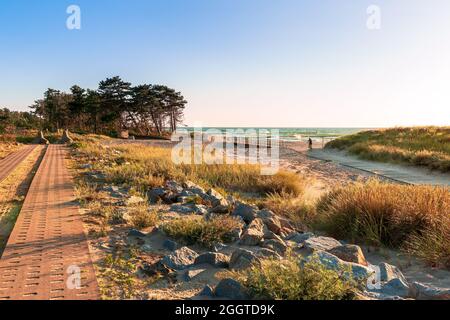 Piste cyclable le long de la côte de la mer Baltique, un beau coucher de soleil sur une plage de sable, des dunes, des herbes ornementales et des rochers de pierre en premier plan, Banque D'Images